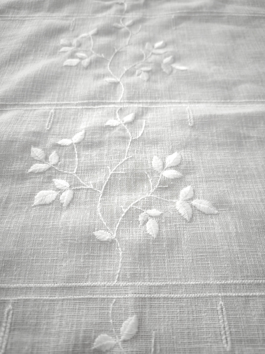 dettaglio ricamo in rilievo della tenda a vetro, con motivo centrale continuativo a rami e foglie su tessuto bianco effetto lino