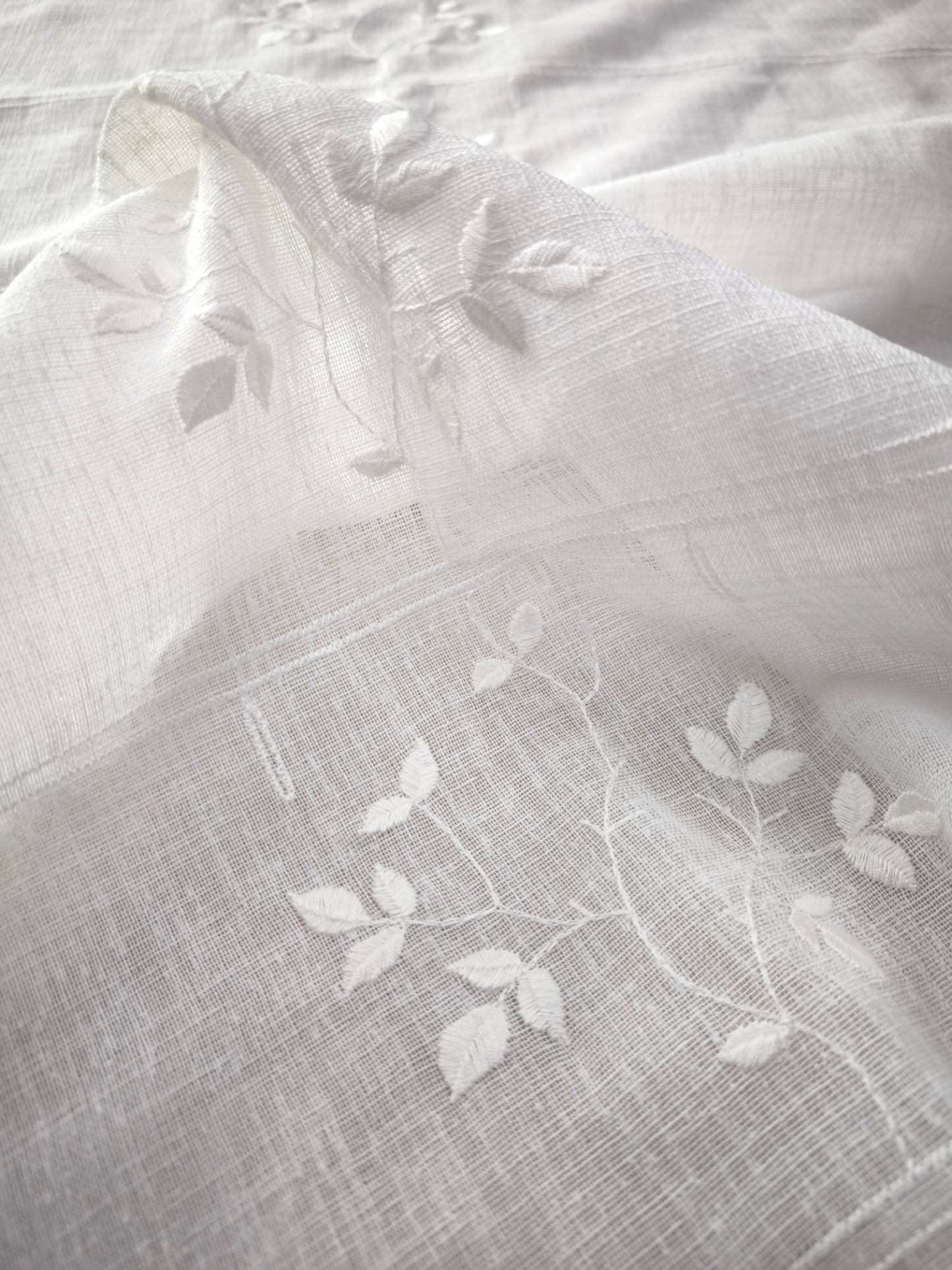 primo piano del ricamo in rilievo a rami e foglie sulla tenda a vetro bianca, dettaglio decorativo elegante su tessuto effetto lino