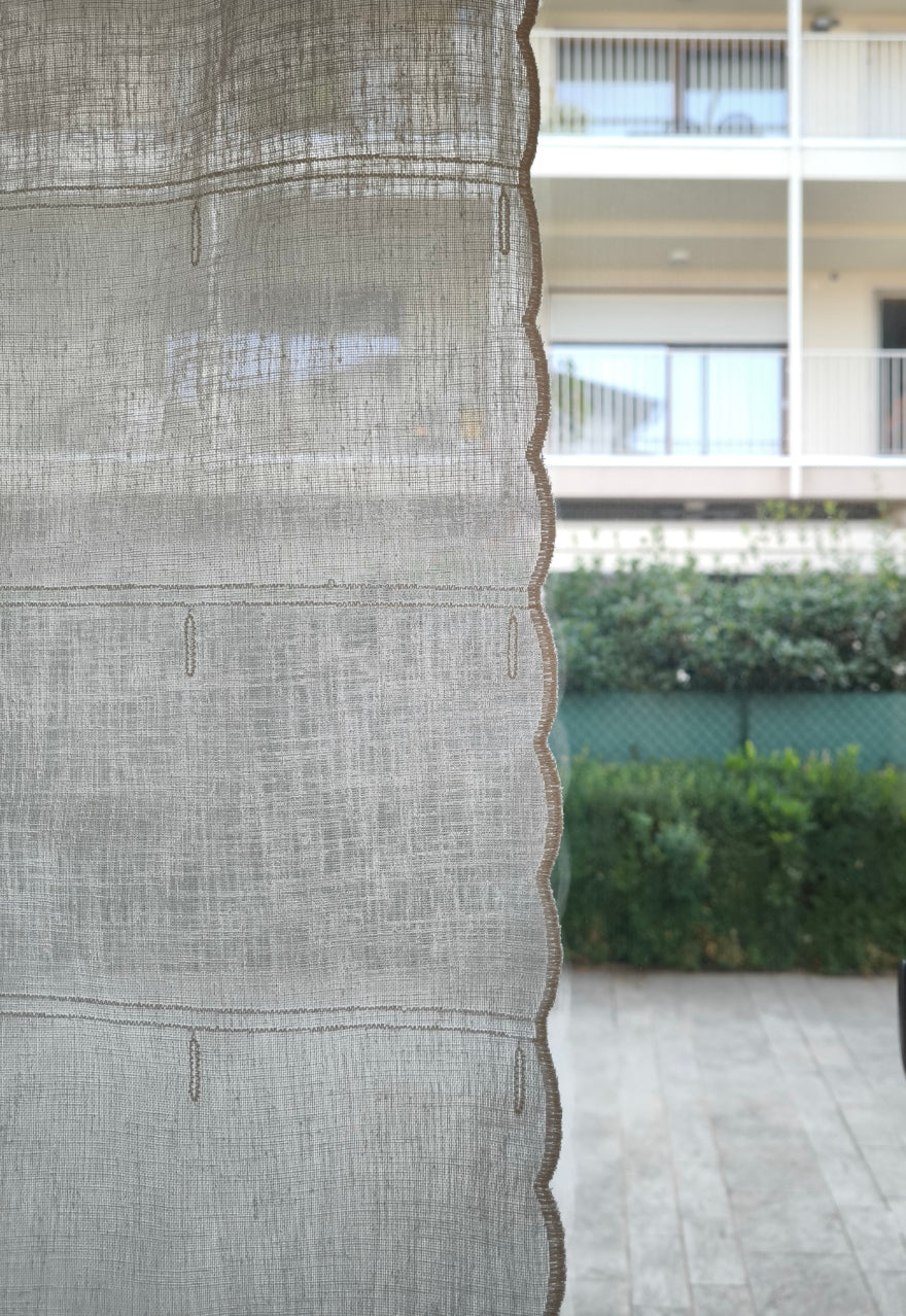 tenda a vetro bianca con ricamo centrale, dettaglio della trasparenza del tessuto effetto lino che lascia filtrare la luce naturale