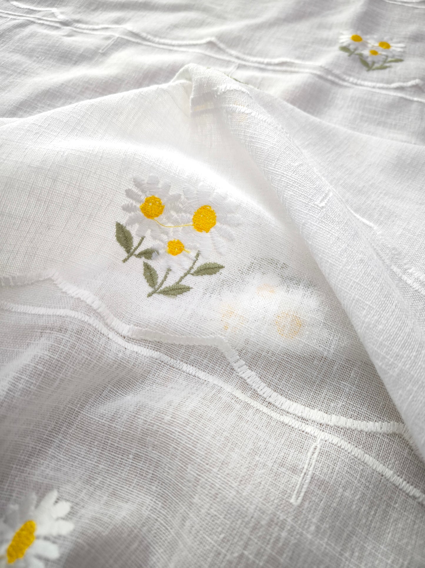 Primo piano ricamo margherita bianca e gialla con gambo verde su tessuto bianco naturale