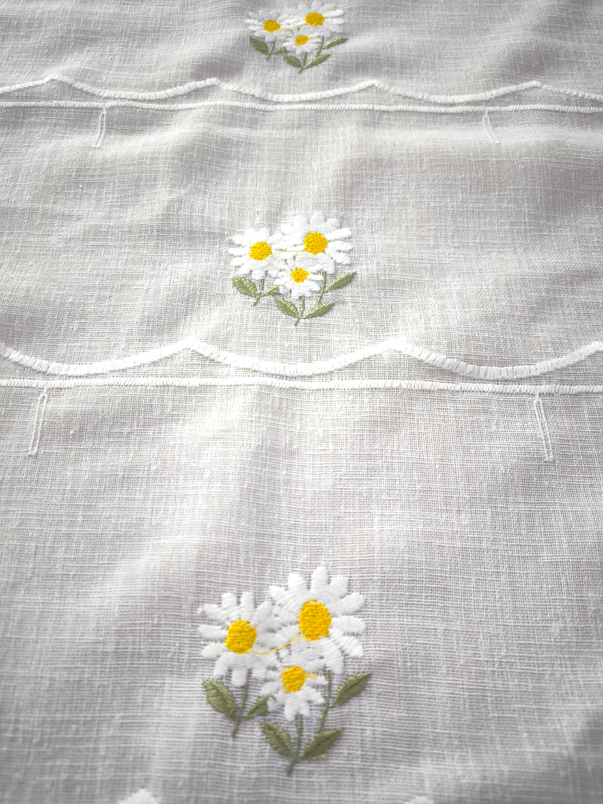 Dettaglio ricamo fiore margherita bianca e gialla con gambo verde su tenda a vetro