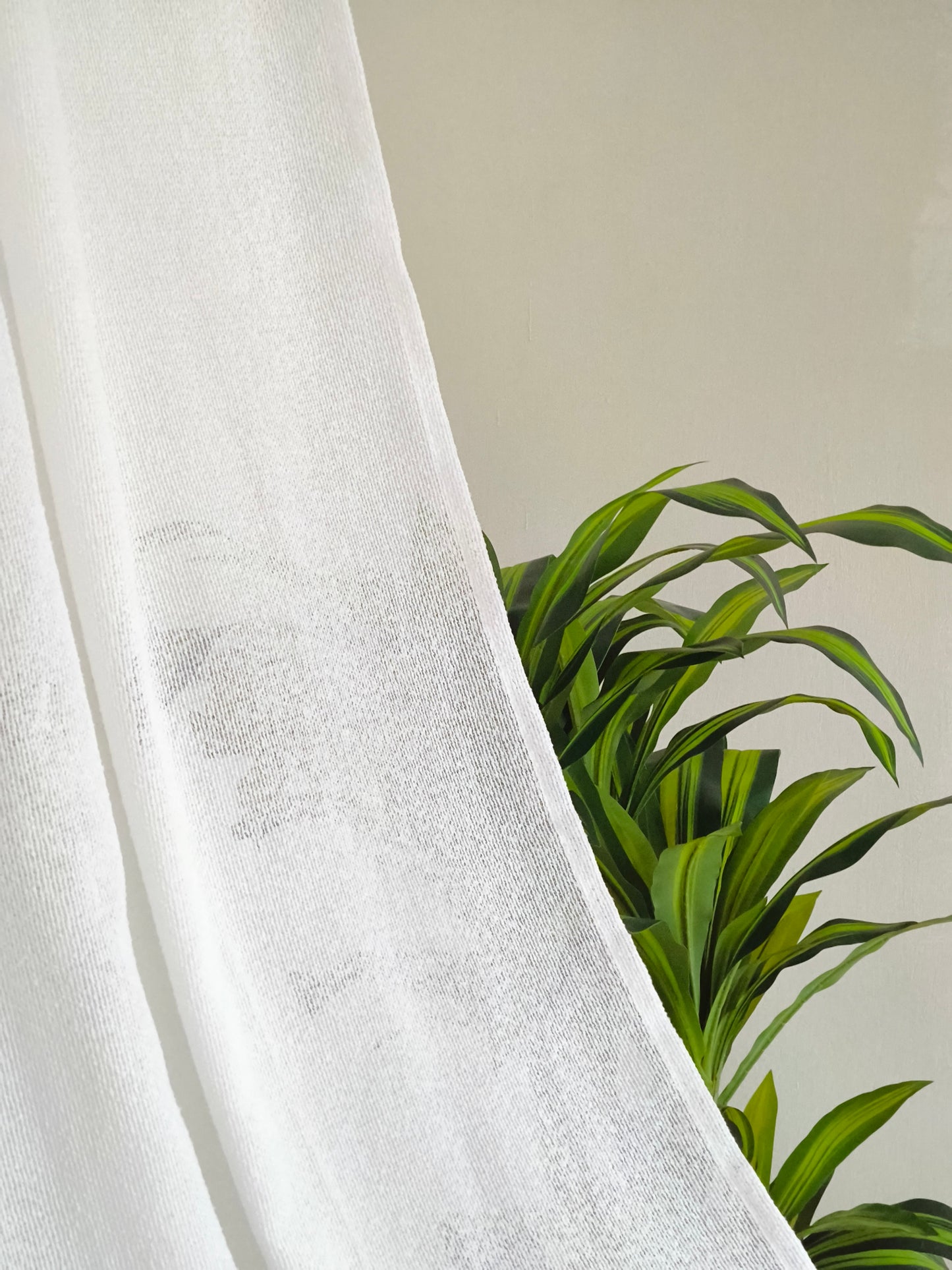 Tessuto bouclé semitrasparente appeso davanti a una pianta, che mostra la sua leggerezza e trasparenza.